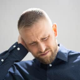 man in blue shirt holding ear looking down in pain