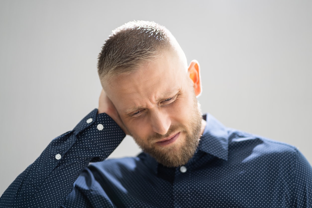 man in blue shirt holding ear looking down in pain
