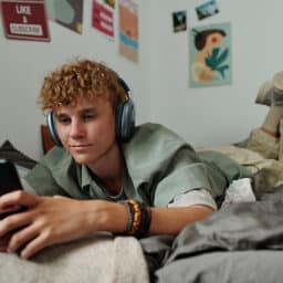 Teenager listening to music through over-ear headphones on their bed.