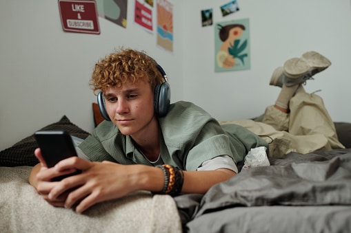 Teenager listening to music through over-ear headphones on their bed.